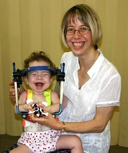 A smiling woman holds a laughing child wearing a medical head brace, both appearing joyful and happy.