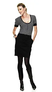 A woman in a striped top and black skirt with hands in pockets, wearing black tights and boots, poses against a white background.