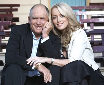 Two people sitting close together, smiling, in a casual outdoor setting.