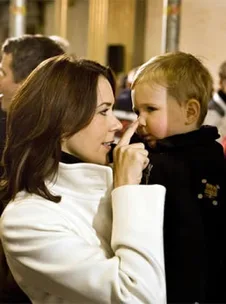 Adult in white coat gently touching toddler's nose at indoor event, both engaged in a tender moment.