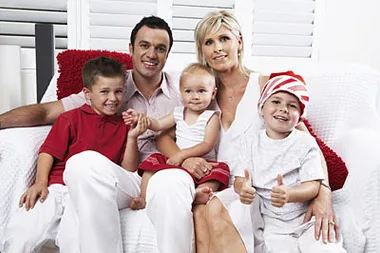 Family sitting on a white couch: two adults and three children wearing festive red and white outfits, smiling together.