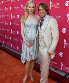 A couple poses on the red carpet at an event, with the woman in a light dress and the man in a light suit.
