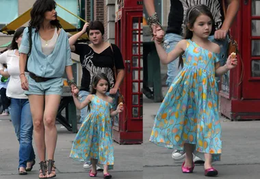 "Child in a colorful dress holding woman's hand, walking on the street, both looking ahead."