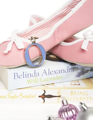 Pink ballet flats with a monogram keychain atop books by Belinda Alexandra and Barbara Taylor Bradford, with ornaments.