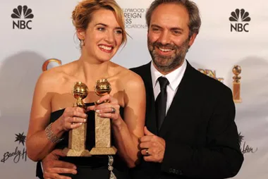 Woman in black dress holding two Golden Globe awards, standing with man in suit at 2009 Golden Globes.