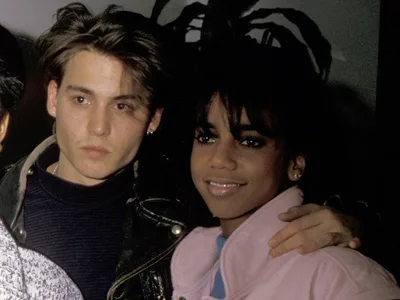 Two people posing together, one with short dark hair and a leather jacket, the other with long hair and a pink jacket, smiling.