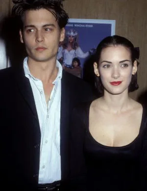 A man in a suit and a woman in a black dress stand together at an event, looking off-camera.