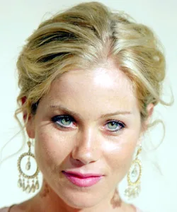 Blonde woman with updo hairstyle, wearing large circular earrings, smiling gently at the camera.