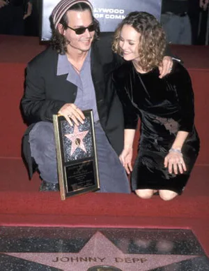 Man in sunglasses holding a Hollywood Walk of Fame plaque, kneeling beside a woman, star on ground says "Johnny Depp".