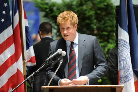 Prince Harry speaking at a podium with flags in the background.