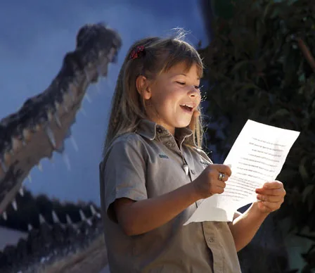 Young child reading a paper, smiling, with a large crocodile image in the background.