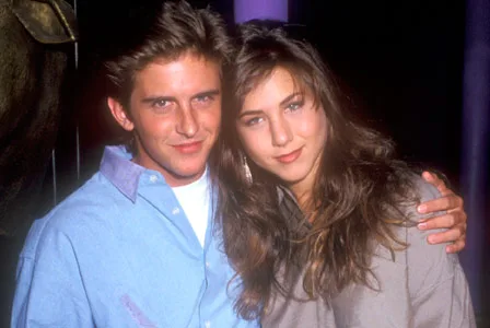 Young woman and man posing together, smiling with arms around each other in a casual setting.