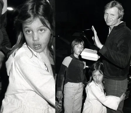 Young child hugging a man's leg, with another child standing nearby, all in a candid, black-and-white photo.