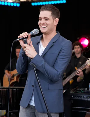 Singer in a blue blazer performs on stage with a band, holding a microphone and smiling.