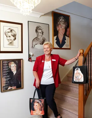 A woman stands by a staircase with framed photos of Princess Diana on the wall and two bags featuring Diana's image.