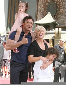 Man holding a child on his shoulders, standing with a woman and another child in front of a decorated building.