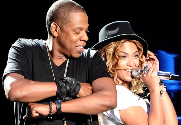 "Two performers on stage, one singing with a microphone and wearing a hat, while the other dances beside them."