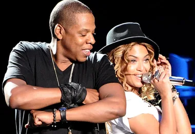 "Two performers on stage, one singing with a microphone and wearing a hat, while the other dances beside them."