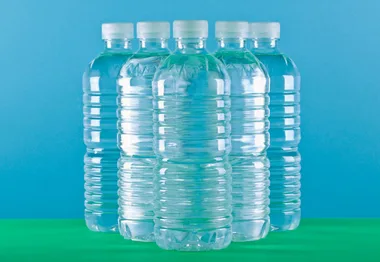 Six clear plastic water bottles on a green and blue background.