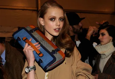 Model holding a colorful, rectangular clutch bag at a fashion event.