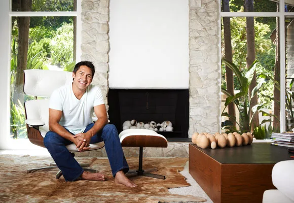 Man sitting in a modern, stylish living room with stone walls, a fireplace, large windows, and plants.