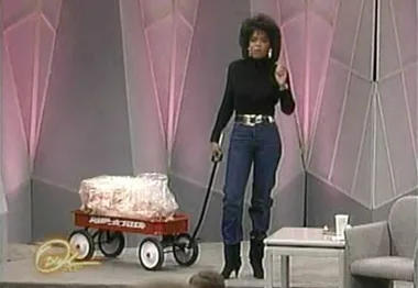 Oprah Winfrey on stage with a red Radio Flyer wagon filled with fat, demonstrating weight loss on her TV show.