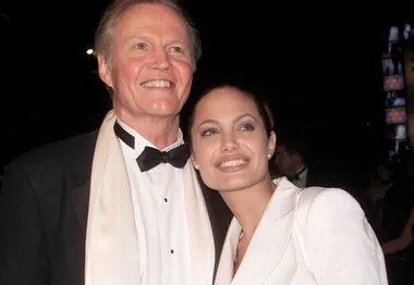 Two people dressed formally, one in a black suit and the other in a white outfit, smiling at an event.