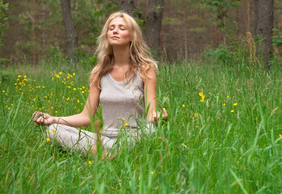 Woman meditating peacefully in a field with green grass and yellow flowers.