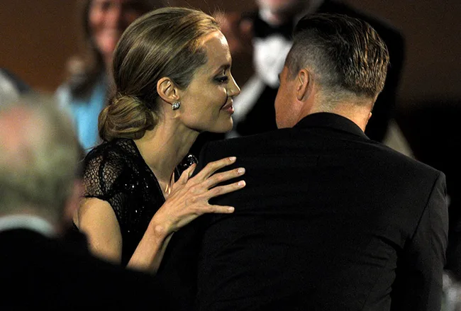 A woman in a black dress embraces a man in a suit at a formal event, both facing away from the camera.