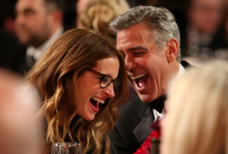Alt text: "Two people laughing together at an event, seated closely and enjoying a joyful moment."