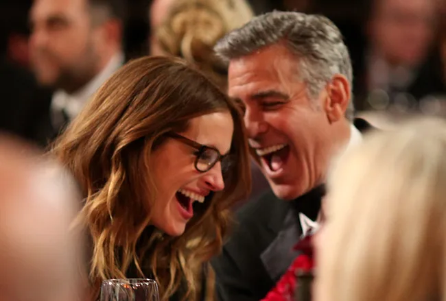 Alt text: "Two people laughing together at an event, seated closely and enjoying a joyful moment."