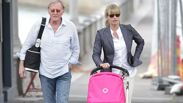 Man and woman walking; woman pushing a pink stroller on a city street.