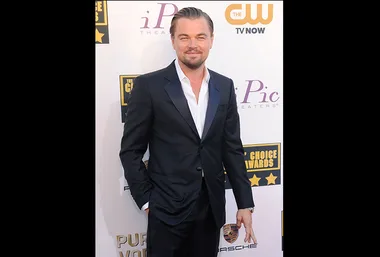 A man in a black suit poses on the red carpet at an award event, with sponsor logos in the background.