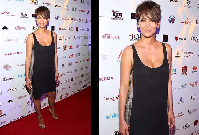 Halle Berry in a black dress at a red carpet event, standing in front of a backdrop with logos.