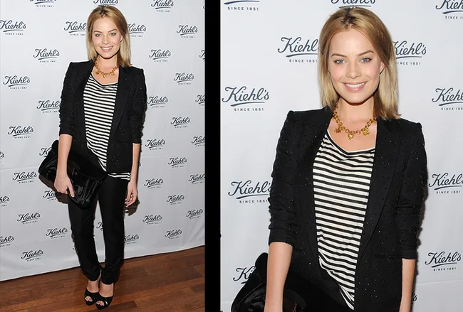 Person in a striped shirt and blazer at a Kiehl's event, holding a clutch, smiling at the camera.