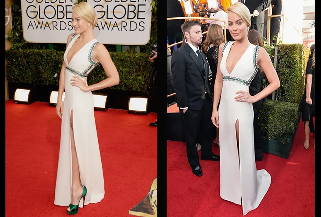 A person in a white dress with green trim poses on the Golden Globe Awards red carpet, hands on hips.