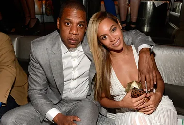 Couple seated together at an event, with the man in a gray suit and the woman in a white dress, smiling at the camera.