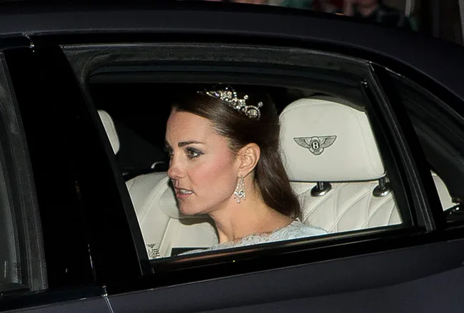 A woman wearing a tiara and earrings sitting in the back seat of a luxury car with a Bentley logo on the headrest.