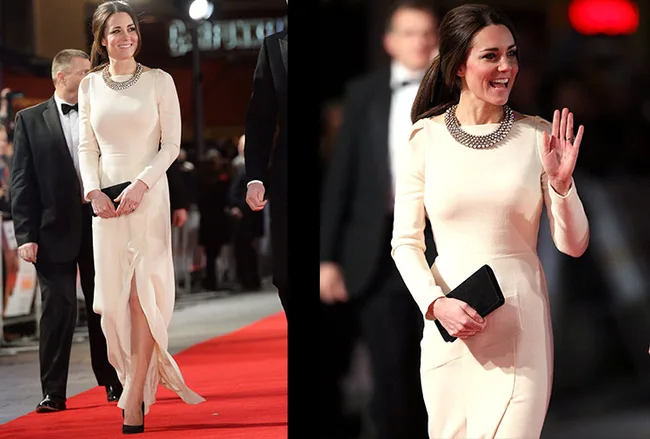 Red carpet event with woman in a white dress with a daring slit, holding a black clutch, surrounded by attendees.