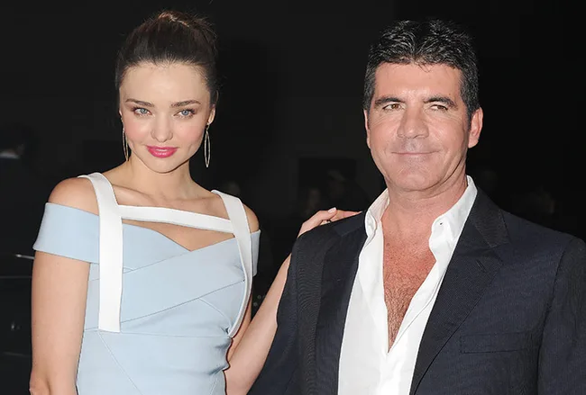 Two individuals posing together; a woman in a blue dress and a man in a black suit.