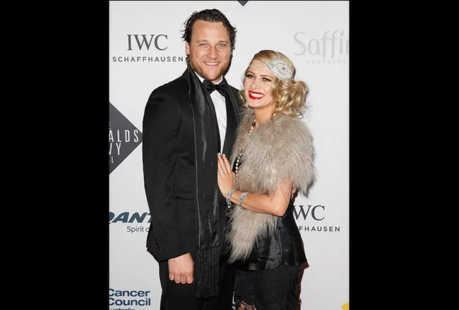A couple in formal attire posing on a red carpet, with a branded backdrop featuring IWC Schaffhausen and Saffire Freycinet logos.