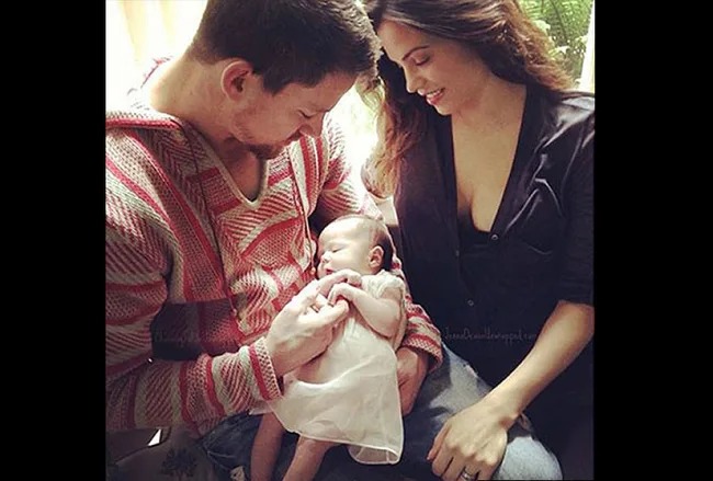 A couple lovingly cradles a baby sitting between them, gazing at the infant with affection in a cozy setting.