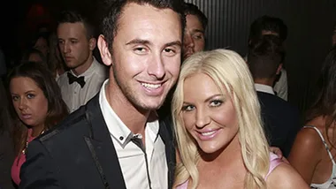 Pair smiling at a party, surrounded by other attendees.