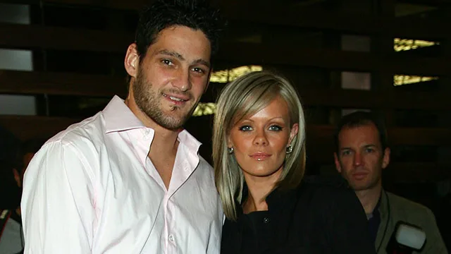 A couple poses for the camera at an event, with onlookers in the background.