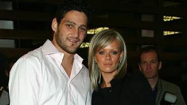 A couple poses for the camera at an event, with onlookers in the background.