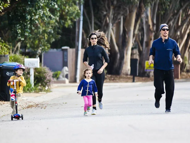 Four people jogging and scootering on a tree-lined street; two adults and two children.