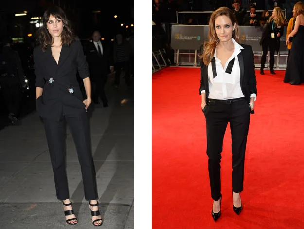 Two women in stylish black suits on red carpet and city street, one in open blazer and shirt, other with floral pin.