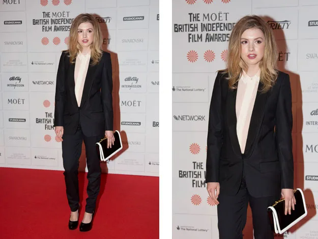Young woman in a black suit on the red carpet at the Moët British Independent Film Awards, holding a white clutch.