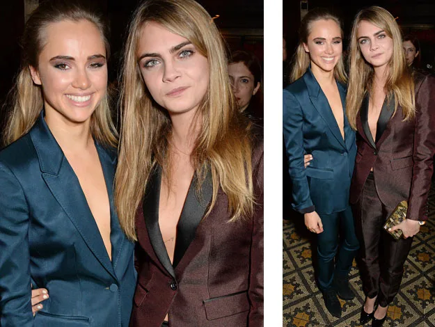 Two women in stylish suits pose together, one in teal and the other in maroon, at an indoor event.