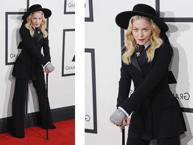 Person in a black suit and hat, holding a cane, posing on a red carpet event.